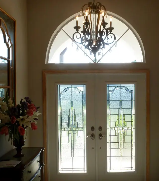 Double entry doors with leaded decorative glass under an arched transom, installed by Strictly Doors